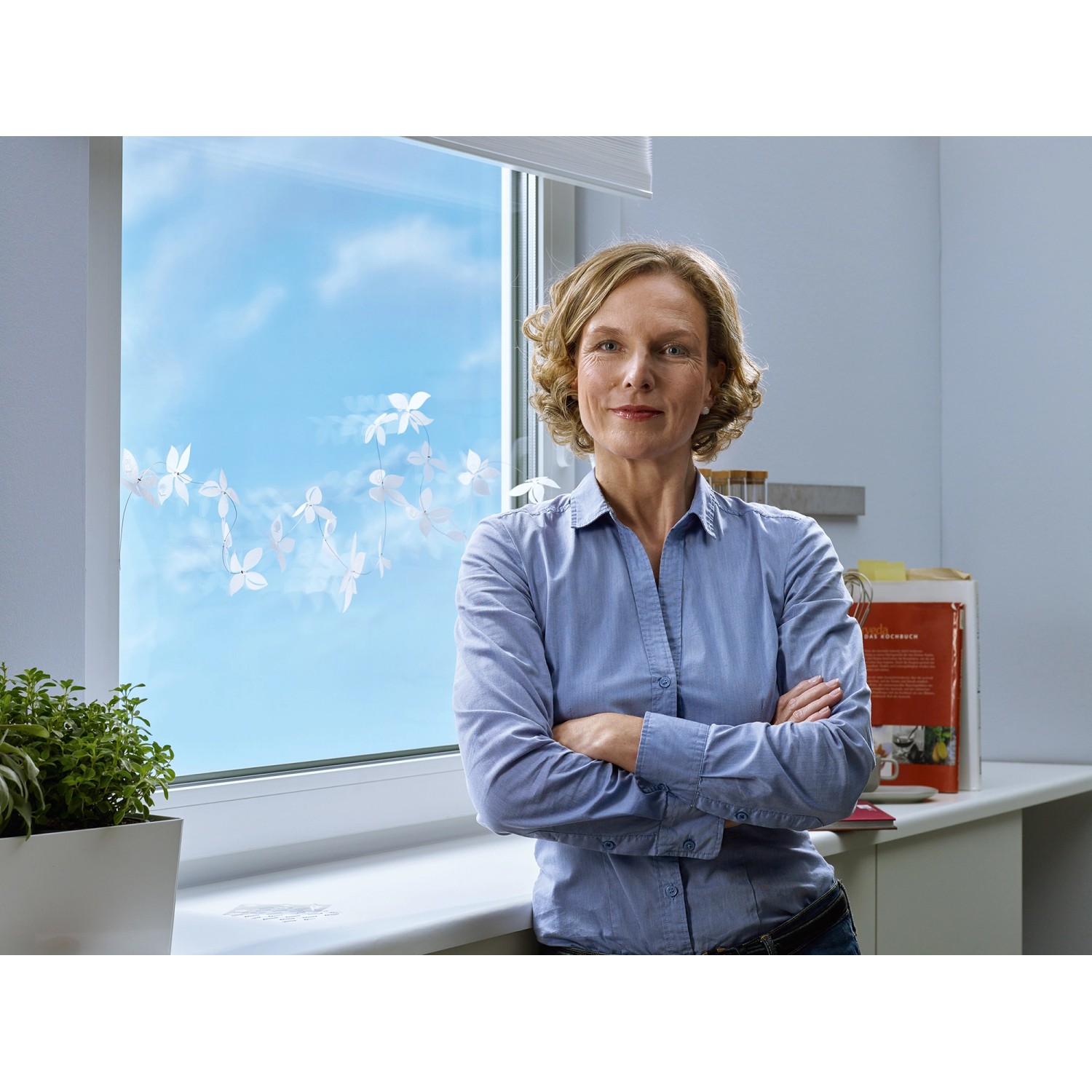 Frau lehnt am Fenster, dekoriert mit Tesa Klebepads für Glas. Temporäre, transparente Befestigung.