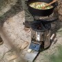 Petromax Raketenofen mit Grillplatte und Kochkreuz im Einsatz mit Topf. Grillutensil für Outdoor-Küche.