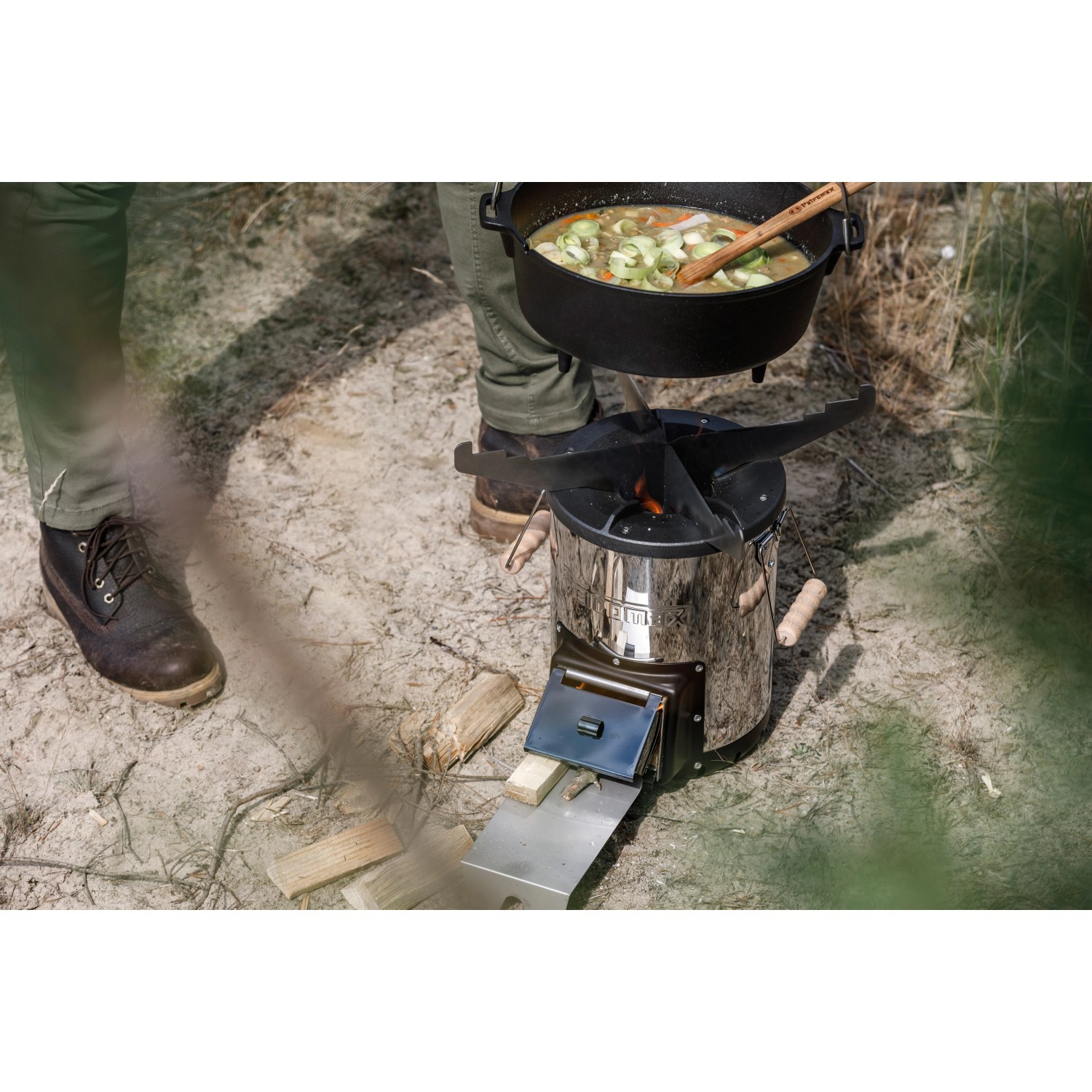 Petromax Raketenofen mit Grillplatte und Kochkreuz im Einsatz mit Topf. Grillutensil für Outdoor-Küche.