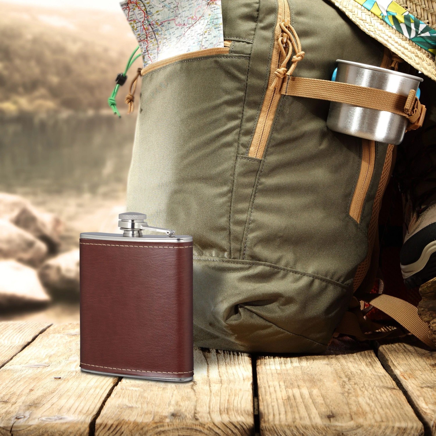 Brauner Edelstahl-Flachmann mit Kunstlederhülle und Bügelverschluss auf Holztisch vor Rucksack. Camping Zubehör.