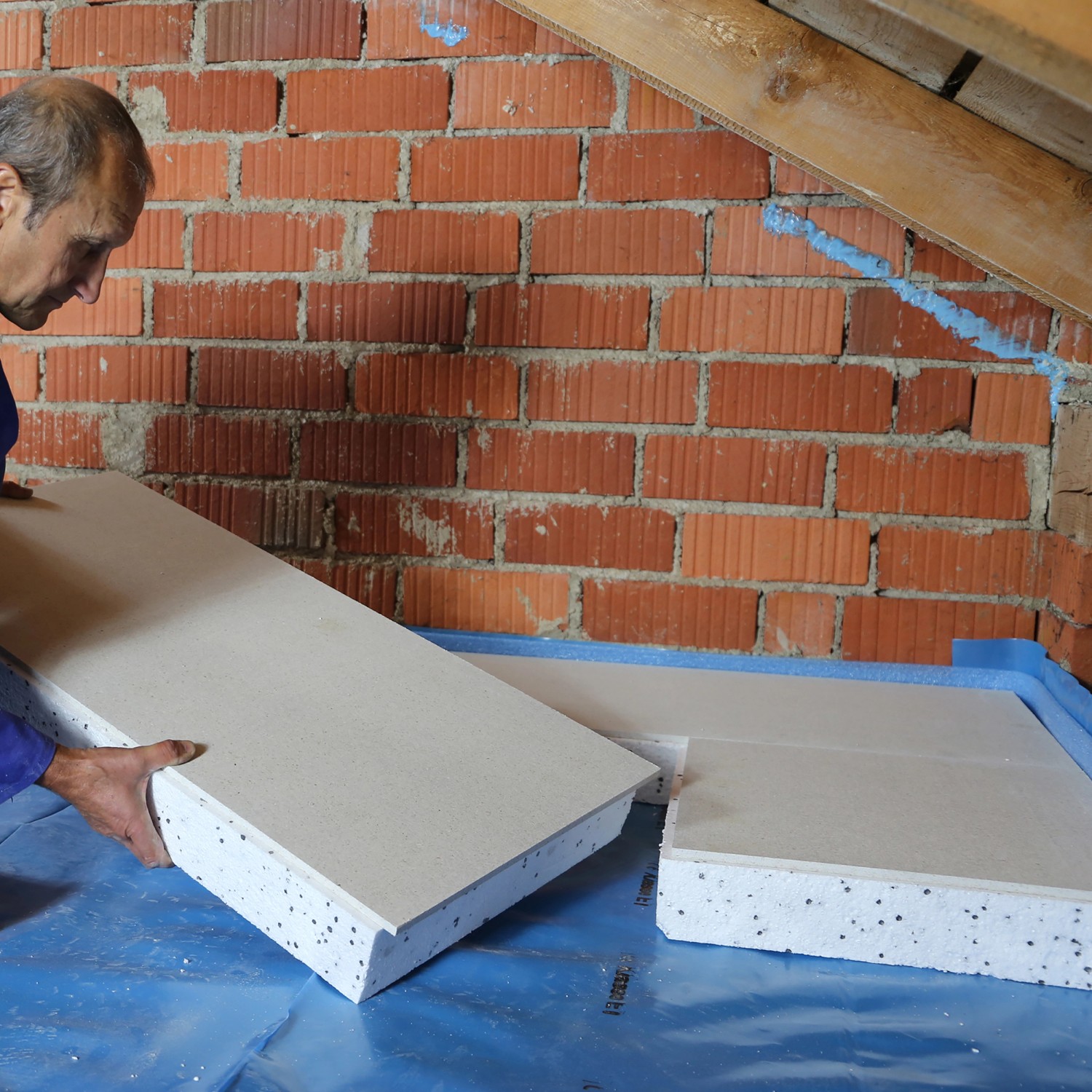 Mann verlegt EPS Dachboden-Dämmplatte 120 mm. Styroporplatte mit Gipsfaser für Wärmedämmung.