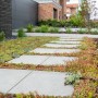 Verlegter Gehweg mit grauen Zementplatten (30x30) und grüner Bepflanzung.