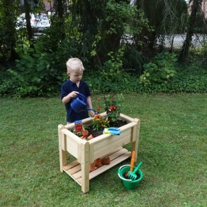 Kind gießt Kräuterbeet Bruno von Promadino aus Holz im Garten.