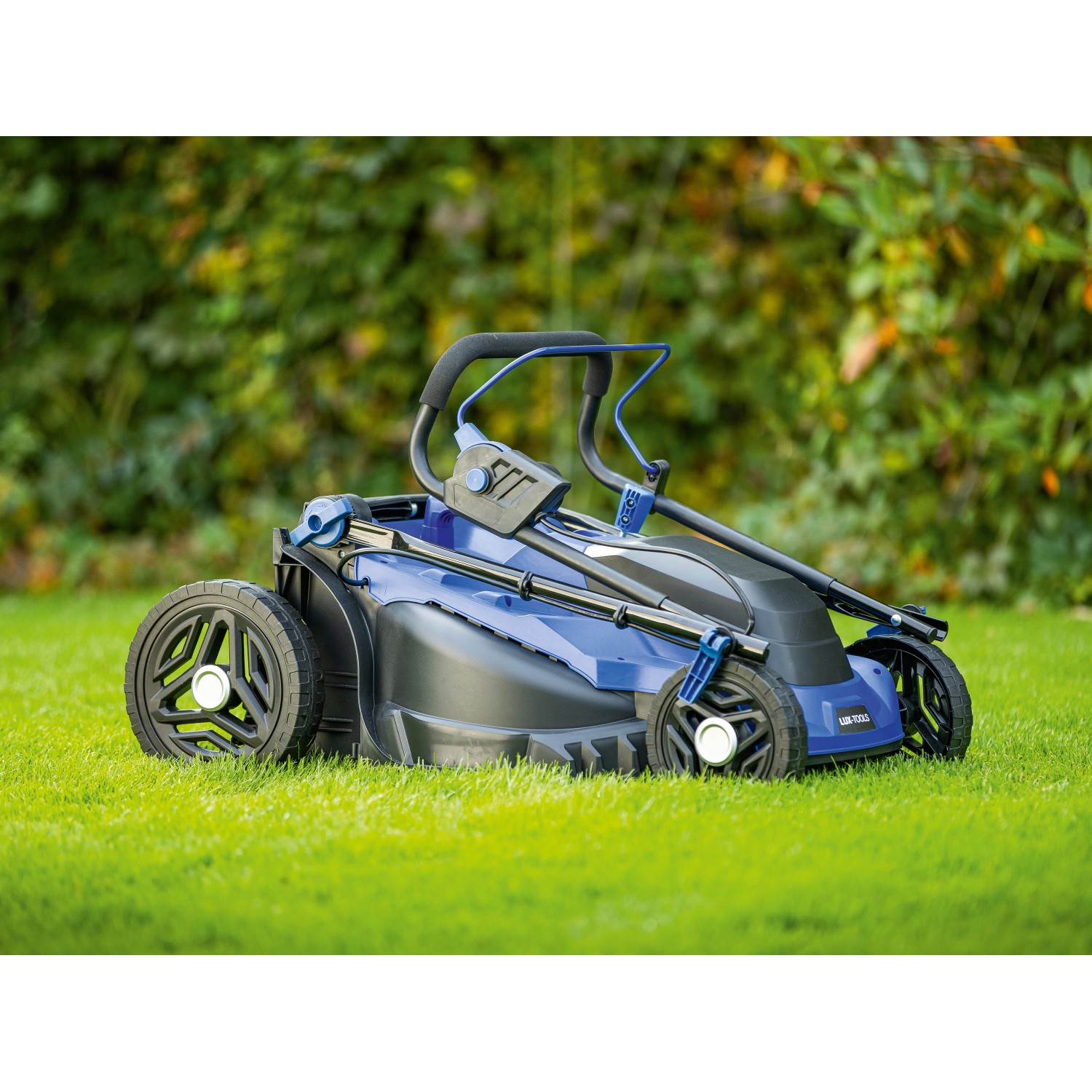 Blauer LUX-TOOLS Elektro-Rasenmäher E-RM-1800/43 auf Rasen. Kompakter Rasenmäher mit verstellbarem Holm.