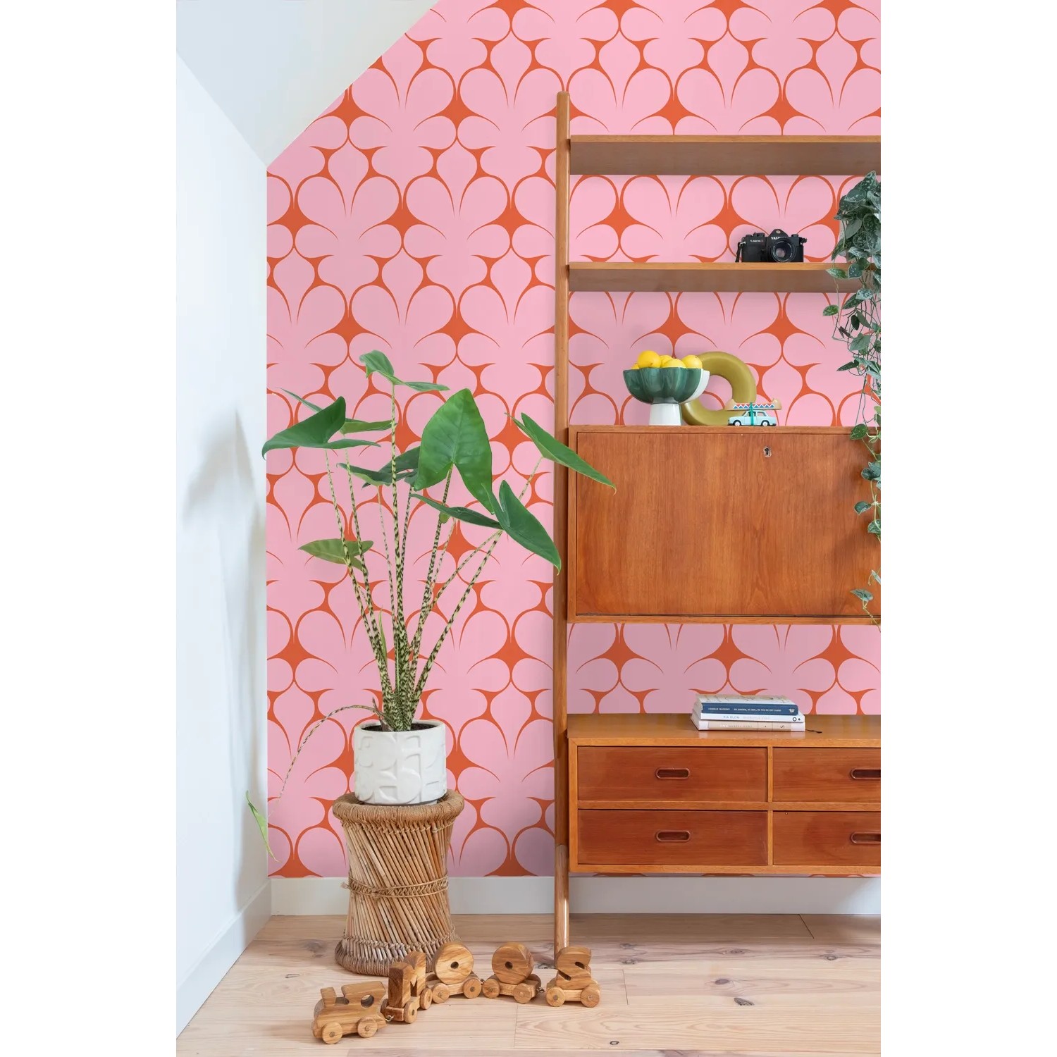 ESTAhome Vliestapete mit rosa-roten Retro-Ornamenten an einer Wand, daneben ein Holzregal und eine Zimmerpflanze.