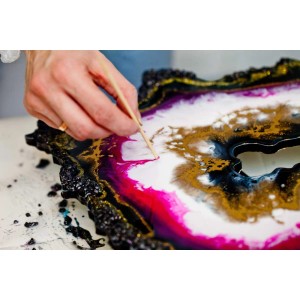 Gießharz-Kunst: Epoxidharz wird mit Werkzeug aufgetragen, um ein farbenfrohes Kunstwerk zu gestalten.