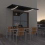 Anthrazitfarbene manuelle Markise mit weißem Rahmen und leuchtenden LEDs über einer Terrasse am Abend.