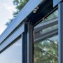 Detail der schwarzen Aluminium-Schiebetür eines Bloomcabin Wandgewächshauses mit Sicherheitsglas und Rollenführung.