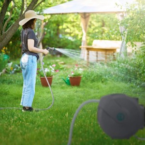 Frau bewässert Garten mit grauem 15m Schlauchaufroller. Automatischer Schlauch, 180° schwenkbar für Gartenbewässerung.