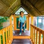Kind auf Zwerkules Spielturm Bolzo mit Rutschen und Schaukel im Garten.