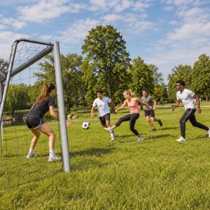 Graues Relaxdays Fußballtor aus Stahl mit PE-Netz auf einer Wiese. Mehrere Personen spielen Fußball. Ideal für Sport & Training.