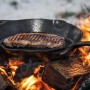 Petromax Grillpfanne aus Gusseisen (30cm) mit Steak über offenem Feuer. Grillutensil für Outdoor-Küche.
