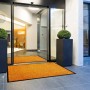 Orange Primaflor Schmutzfangmatte Clean (90x150cm) vor Eingangstür mit Pflanzen.