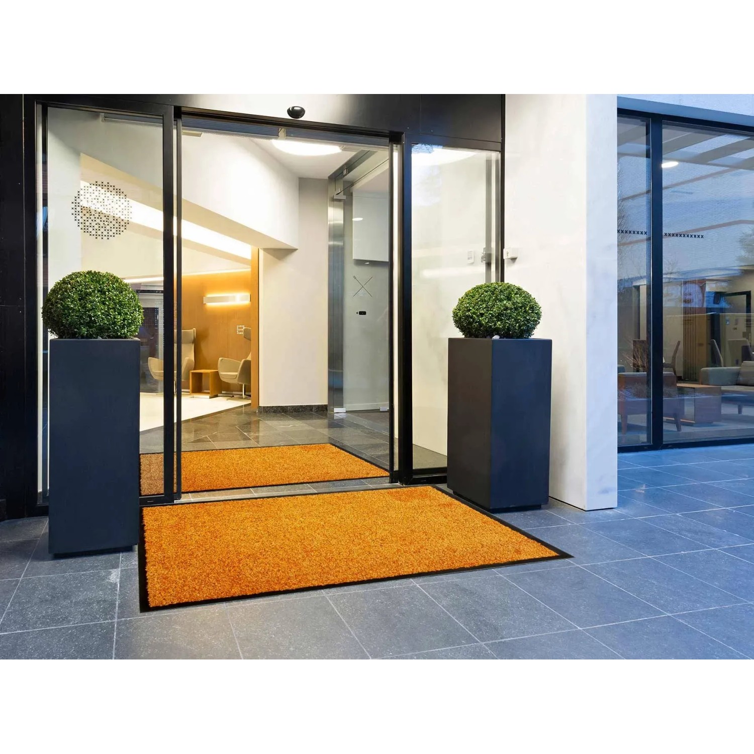 Orange Primaflor Schmutzfangmatte Clean (90x150cm) vor Eingangstür mit Pflanzen.