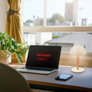 Brilo Tischleuchte Wanda in Coffee-Warmgrey auf Schreibtisch mit Laptop und Smartphone.