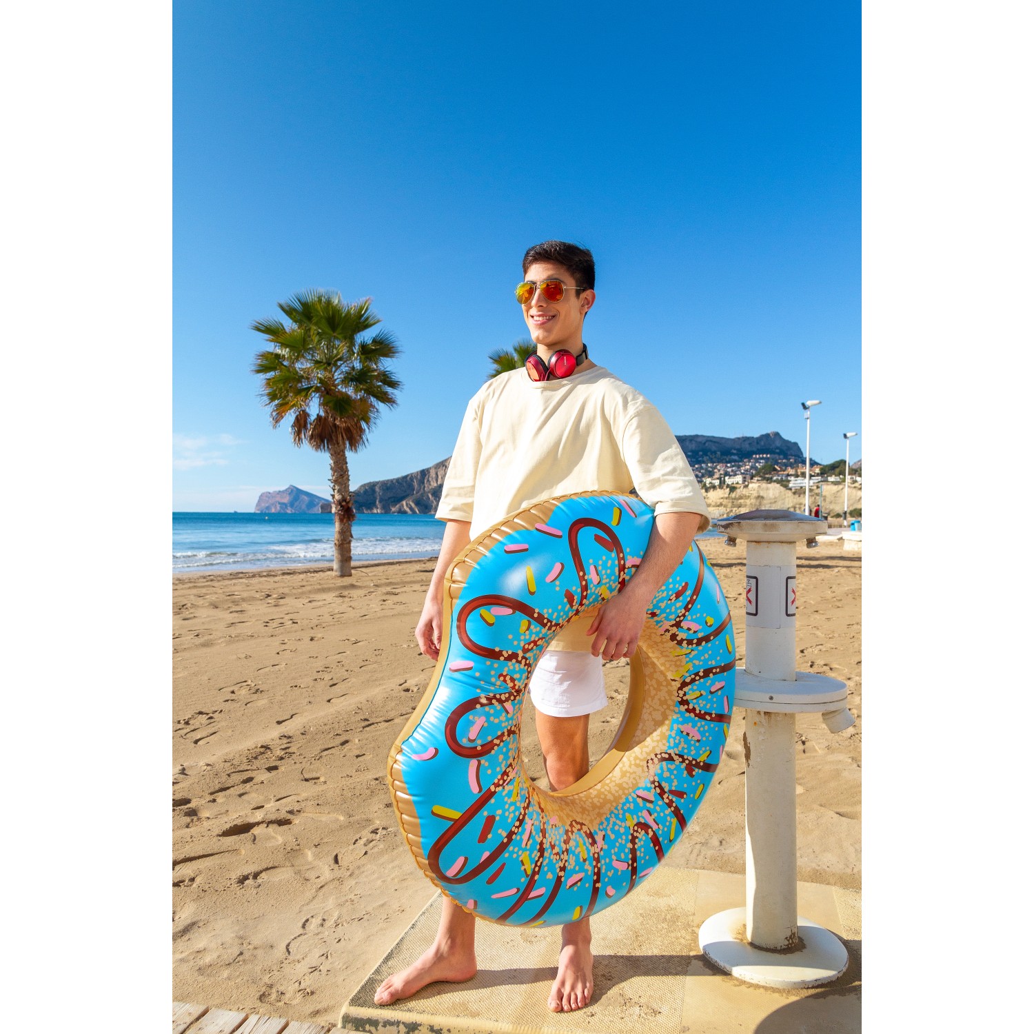 Bestway Schwimmring Donut, Ø 107 cm, blau mit bunten Streuseln, gehalten von Person am Strand.