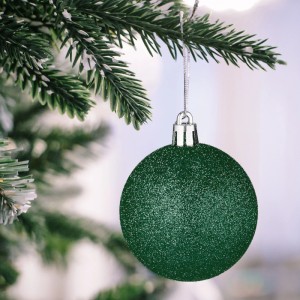 Dunkelgrüne, glitzernde Weihnachtskugel aus bruchsicherem Kunststoff am Tannenbaum. Festlicher Christbaumschmuck.