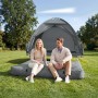 Graues SoBuy Feldbett mit Campingzelt für 2 Personen. Paar sitzt auf Luftmatratze vor dem Zelt im Grünen.