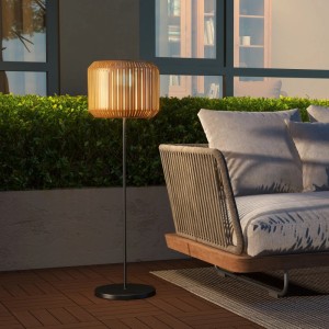 Leuchtende Rattan Solar Außenleuchte mit gelbem Schirm und schwarzem Standfuß auf Terrasse neben Sofa.