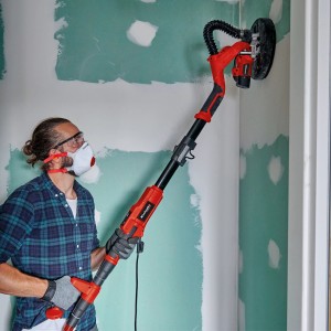 Mann schleift Wand mit Einhell Trockenbauschleifer und Schleifgitter-Set, Ø 225 mm.