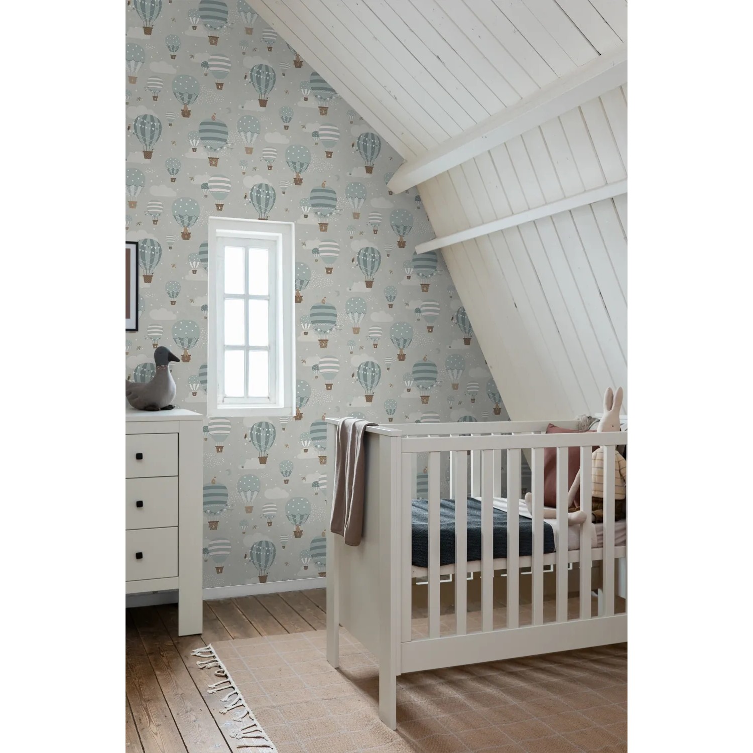 Dekorative Tapete mit blauen Luftballons und Wolken im Kinderzimmer. Weißes Babybett und Kommode.