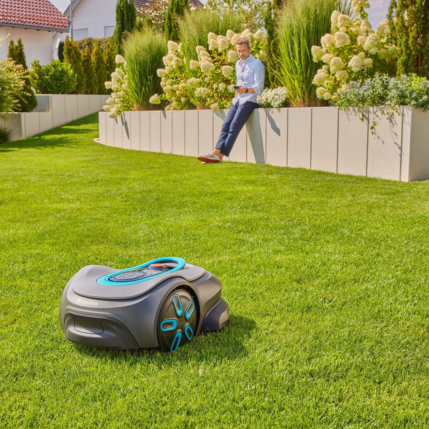 Gardena Smart Sileno Max Mähroboter auf Rasen, Mann sitzt im Hintergrund. Automatische Rasenpflege für bis zu 1.500 m².