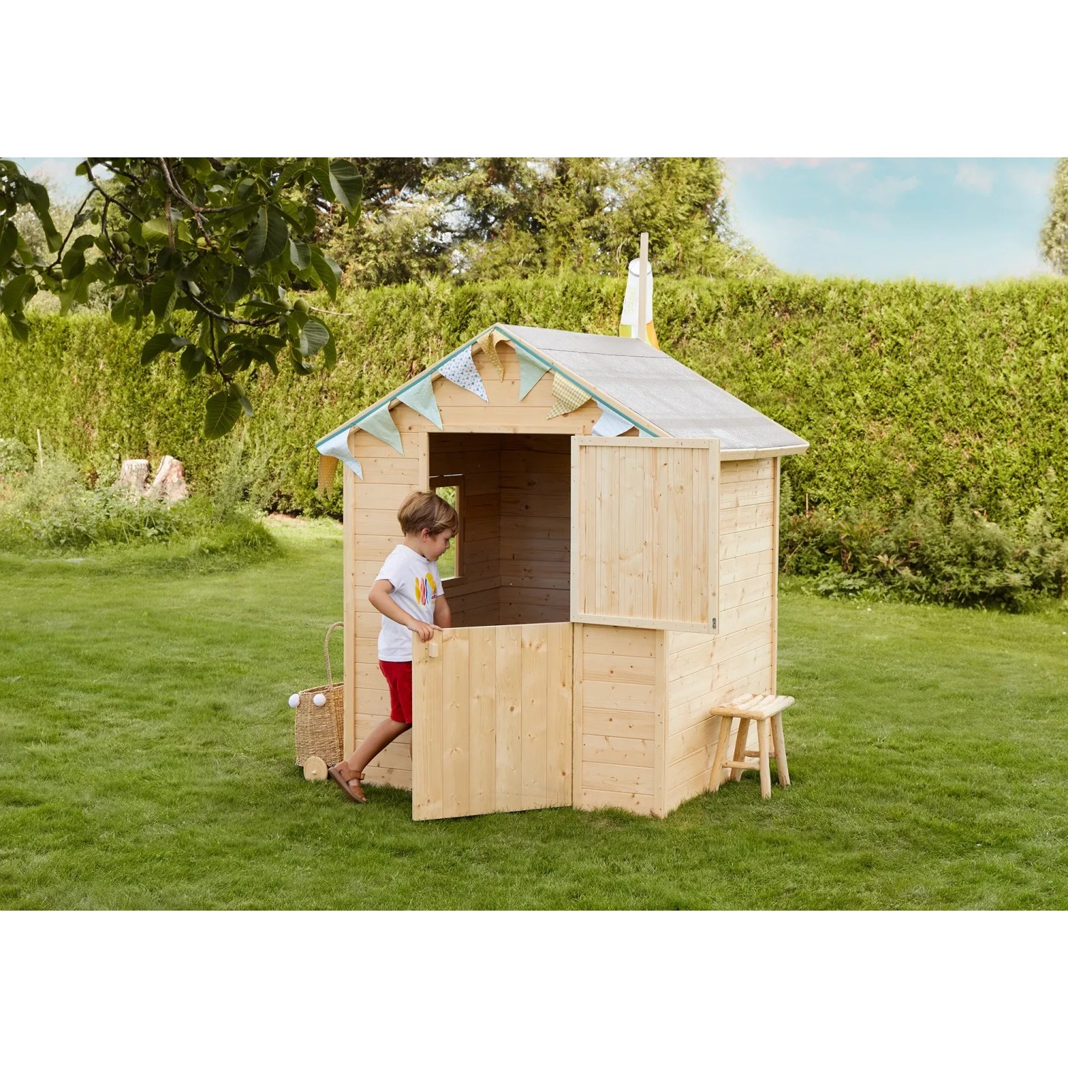 Soulet Kinderspielhaus Garance aus Holz, naturbelassen, mit Fenster und Windsack im Garten.