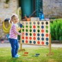 Kind spielt im Garten mit großem Holz Vier Gewinnt Spiel. Naturfarbenes Brett, rote und blaue Spielsteine. XXL Outdoor Spaß.