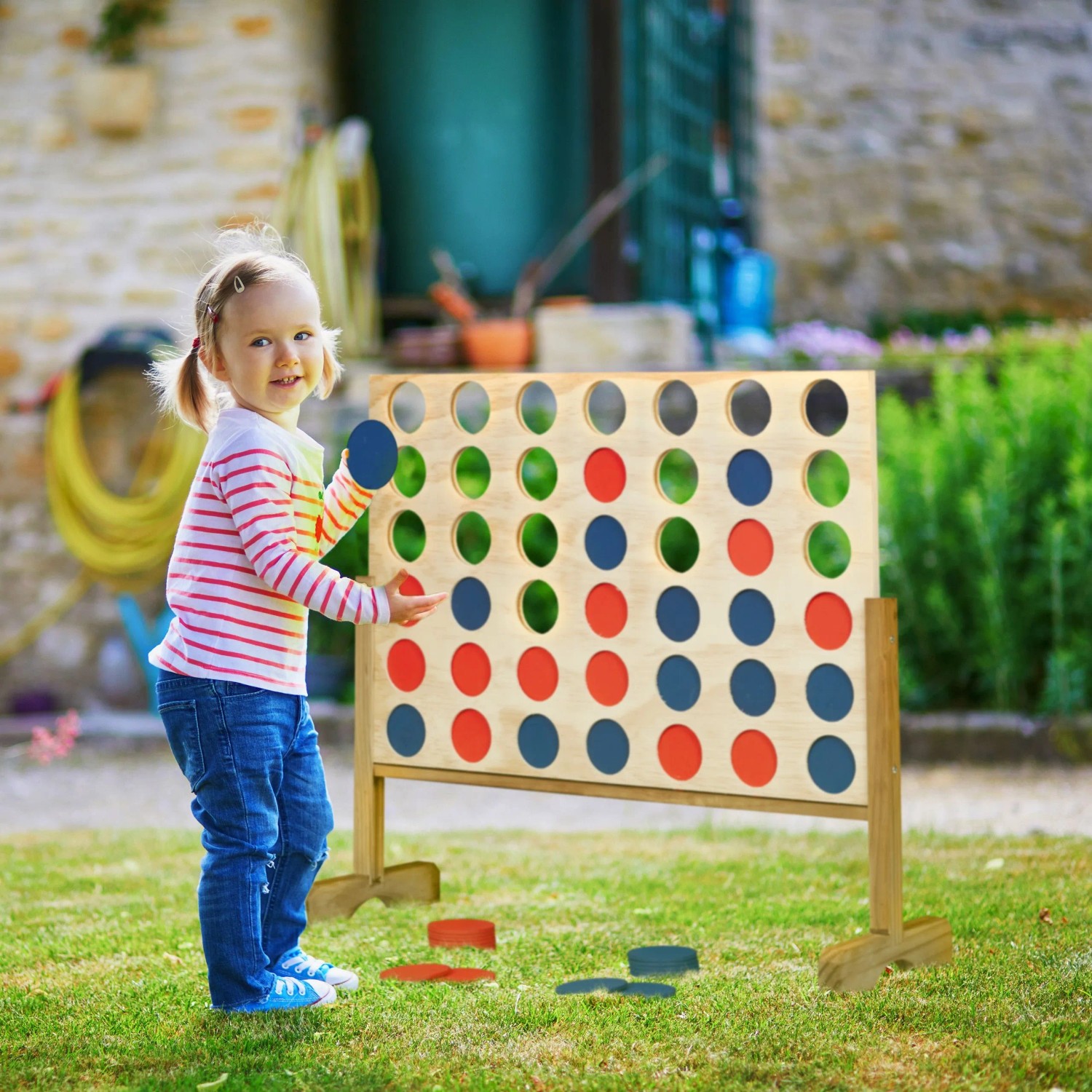 Kind spielt im Garten mit großem Holz Vier Gewinnt Spiel. Naturfarbenes Brett, rote und blaue Spielsteine. XXL Outdoor Spaß.