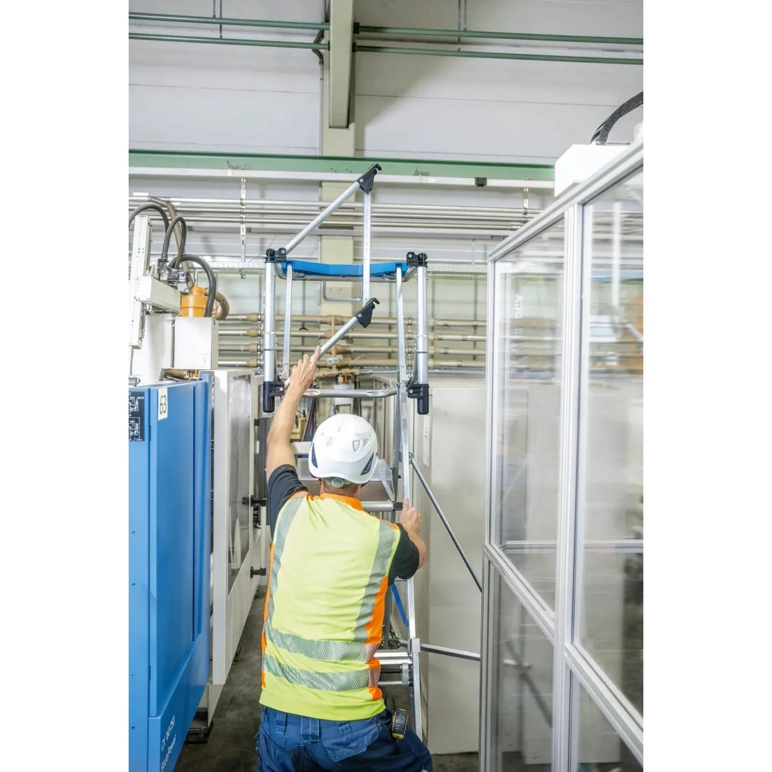 Zarges Teleskop-Plattformleiter ZAP Masterflex Plus mit Mann auf Stufen in Produktionshalle.