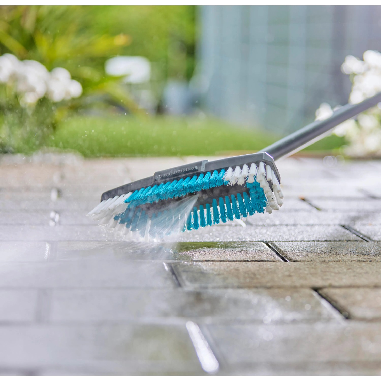 Gardena Cleansystem Stielbürste Hard in Aktion: Reinigung von Pflastersteinen mit Wasser.