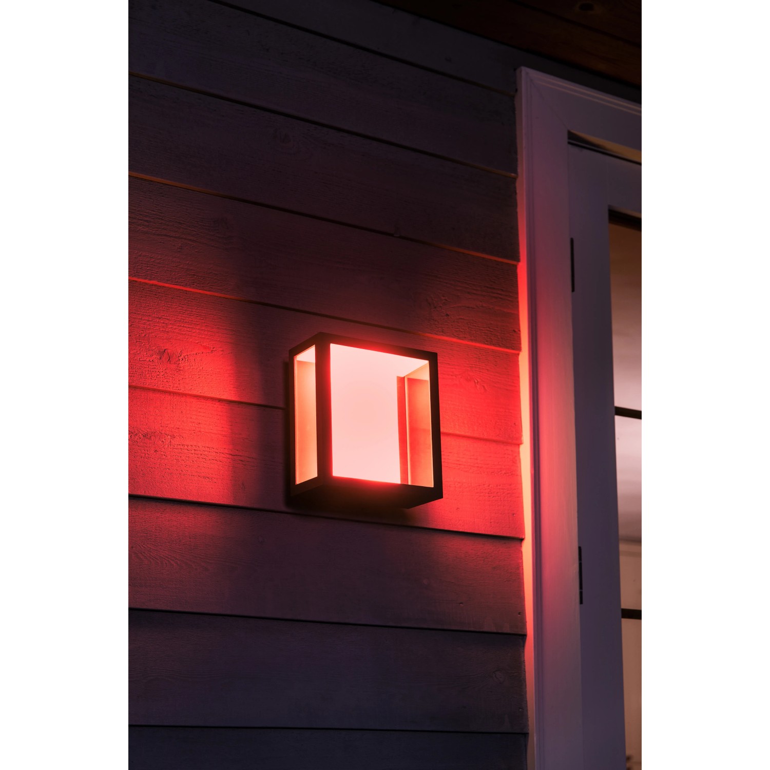 Philips Hue Impress LED-Wandleuchte breit, schwarzes Gehäuse mit rotem Lichtschein an Hauswand.