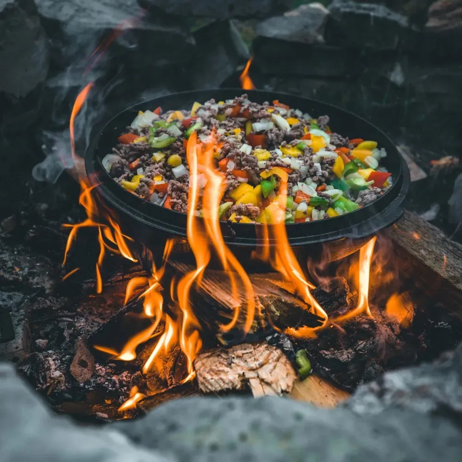 Petromax Dutch Oven FT12 auf offenem Feuer mit Gemüse und Fleisch. Grillutensil für Outdoor-Küche.