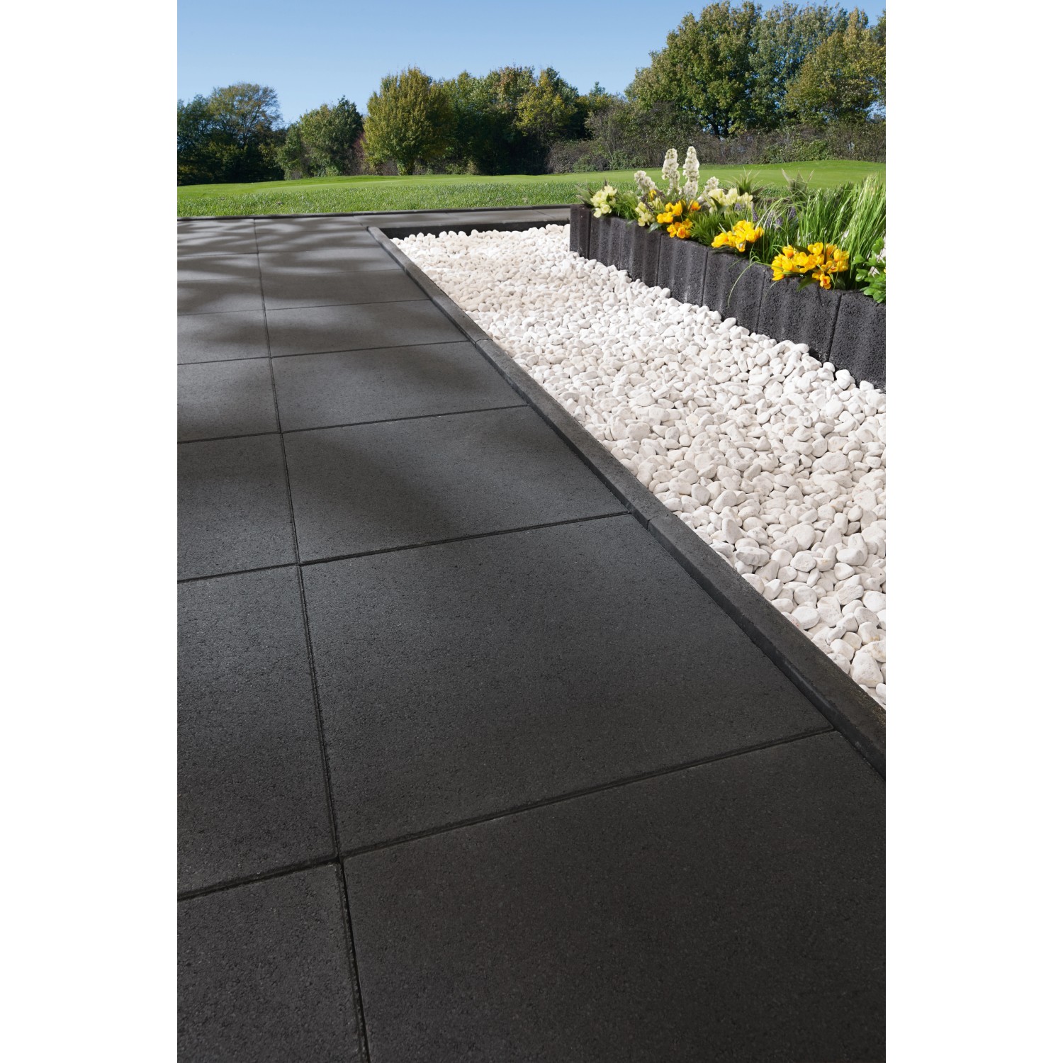 Weißer Marmorkies Carrara (8-16mm) im Gartenbeet neben dunklen Terrassenplatten.