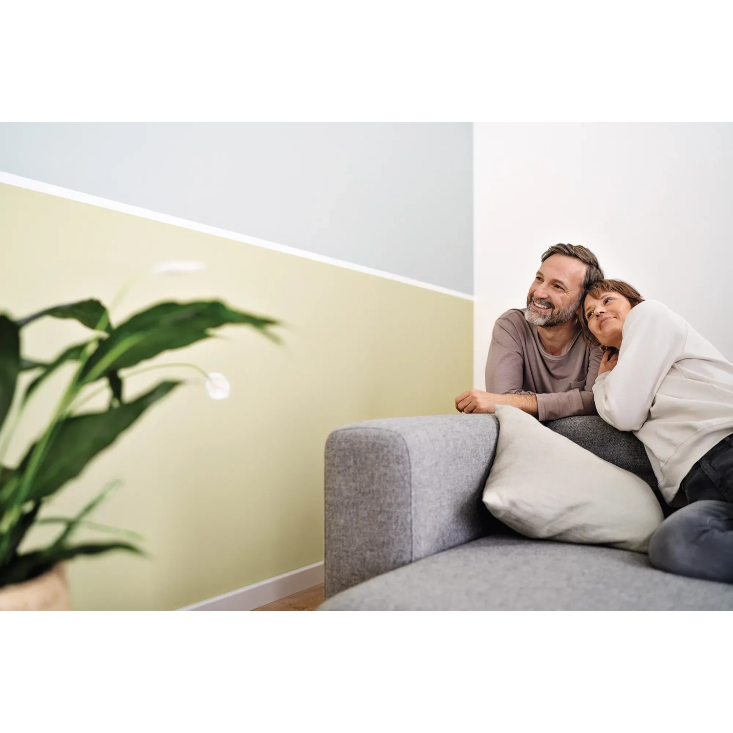 Paar entspannt auf Sofa vor Wand mit Tesa Malerband abgeklebt. Präzise Farbkante.