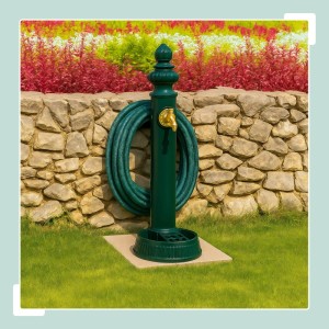 Dunkelgrüner Relaxdays Standbrunnen aus Metall mit Schlauchhalter vor Steinmauer und Blumenbeet.