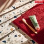 Rote Floordirekt Badematte (60x150) mit Zahnbürste und Tube auf gemustertem Boden.