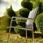 Acamp Stapelsessel Auris aus Edelstahl mit Acatex-Gewebe vor Gartenkulisse.
