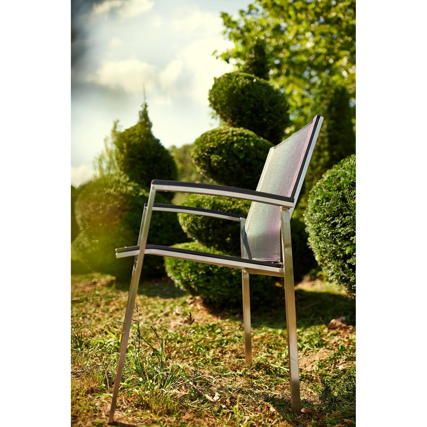 Acamp Stapelsessel Auris aus Edelstahl mit Acatex-Gewebe vor Gartenkulisse.
