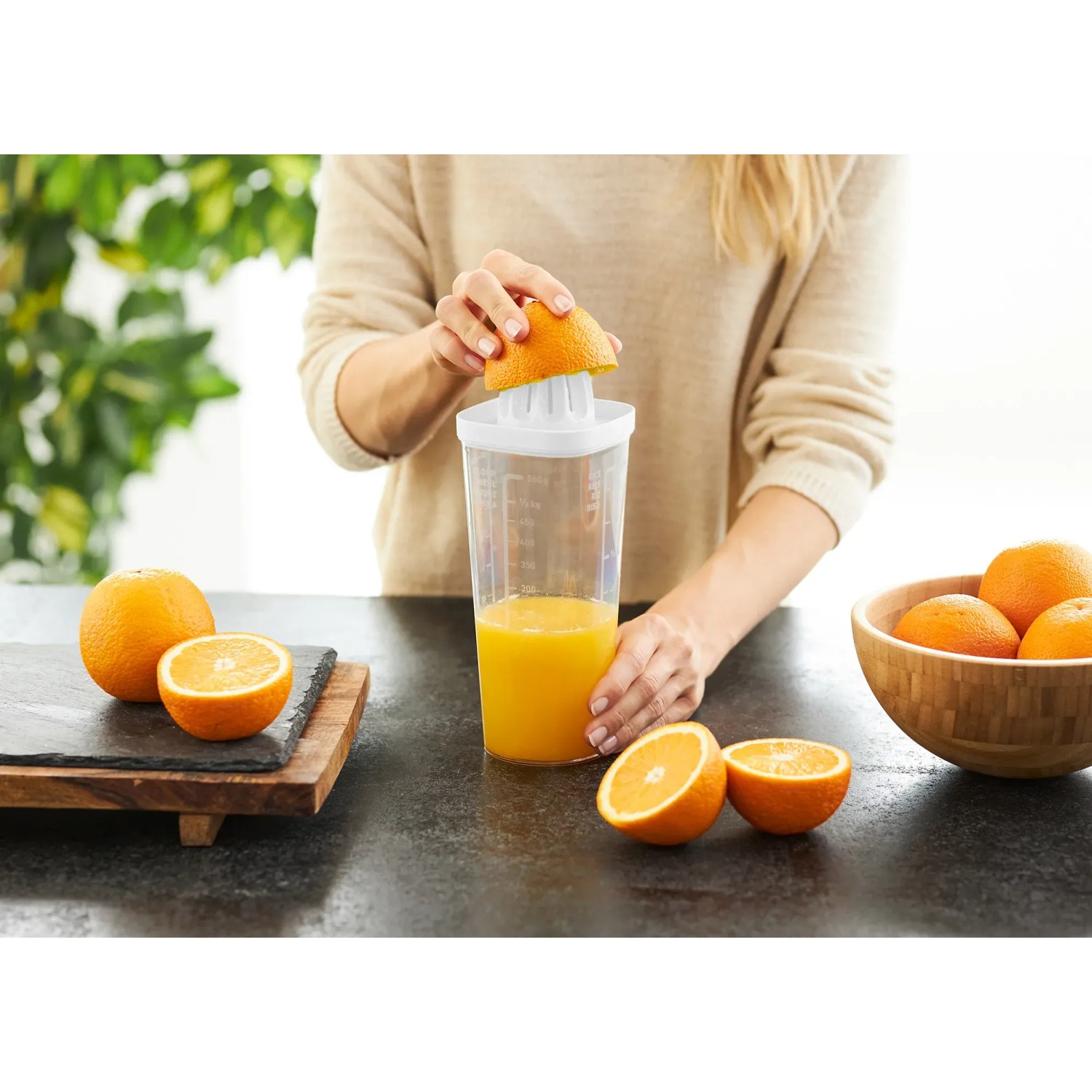 Rotho Küchenhelfer Loft: Frau presst Orange mit dem 5-in-1 Küchengerät, weiß-transparent.
