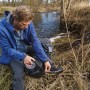 Mann repariert Rucksack mit Tesa Ultra Power Extreme Reparaturband am Fluss.