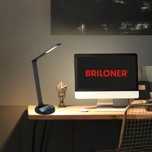 Schwarze Brilo LED-Schreibtischleuchte Cuma mit induktiver Ladefunktion auf einem Schreibtisch.