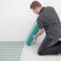 Mann verlegt Perobe elektrische Fußbodenheizung (2 m²) im Raum. Heizmatte mit Heizkabel.