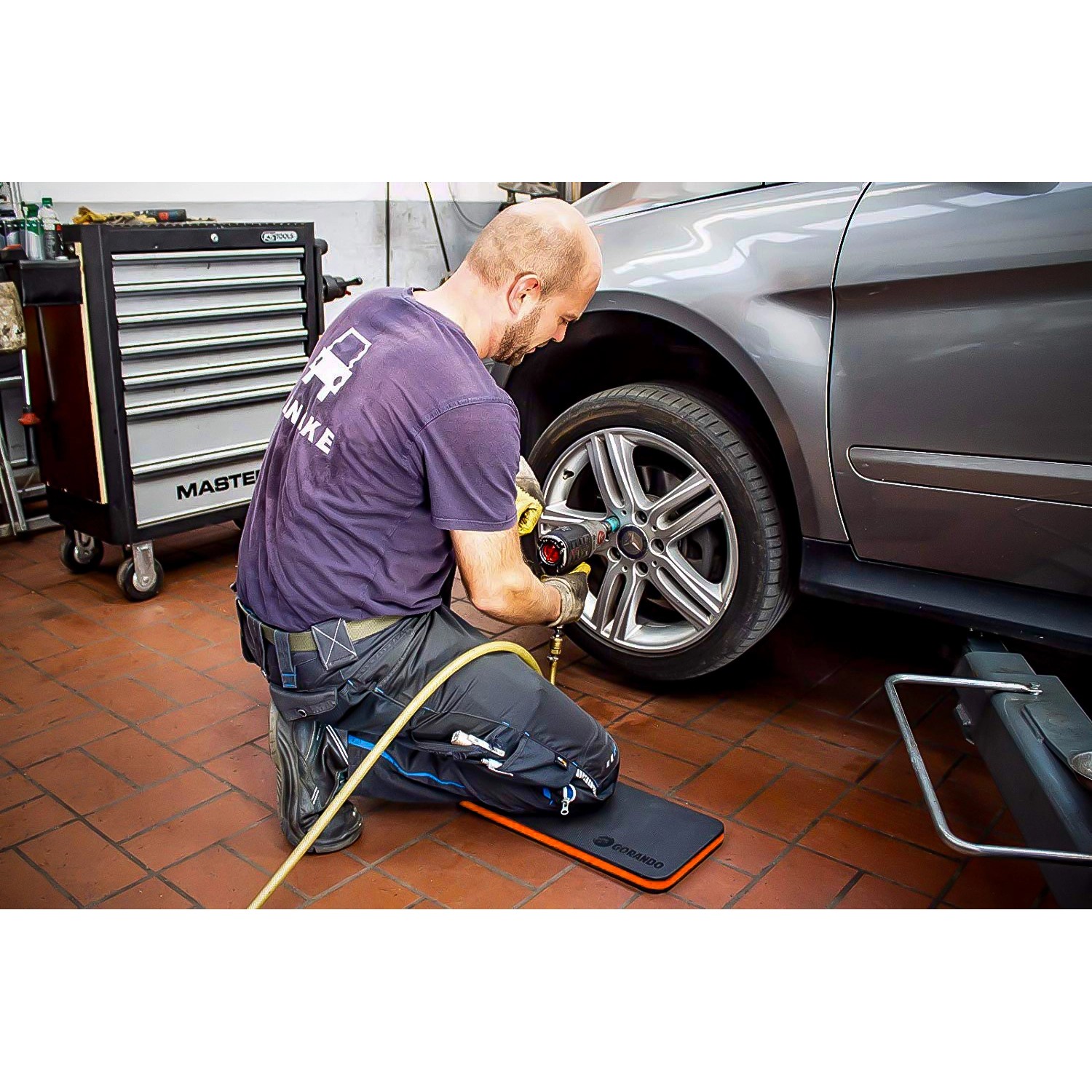 Mann kniet auf Gorando Kniekissen bei Reifenwechsel. Knieschutz für Werkstatt und Garten.