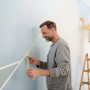 Zwei Personen kleben mit gelbem Tesa Malerband eine Wand für Malerarbeiten ab.