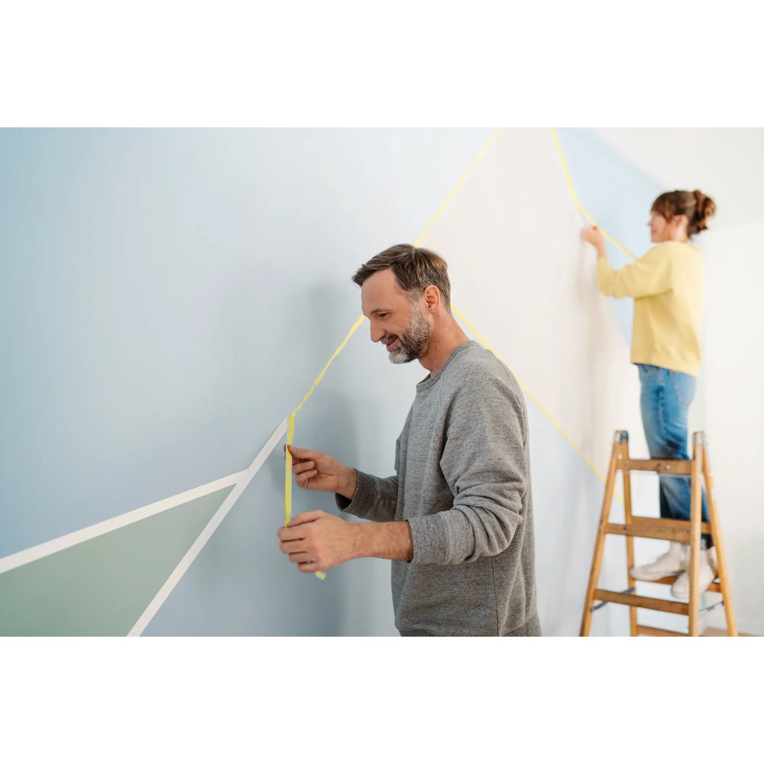 Zwei Personen kleben mit gelbem Tesa Malerband eine Wand für Malerarbeiten ab.