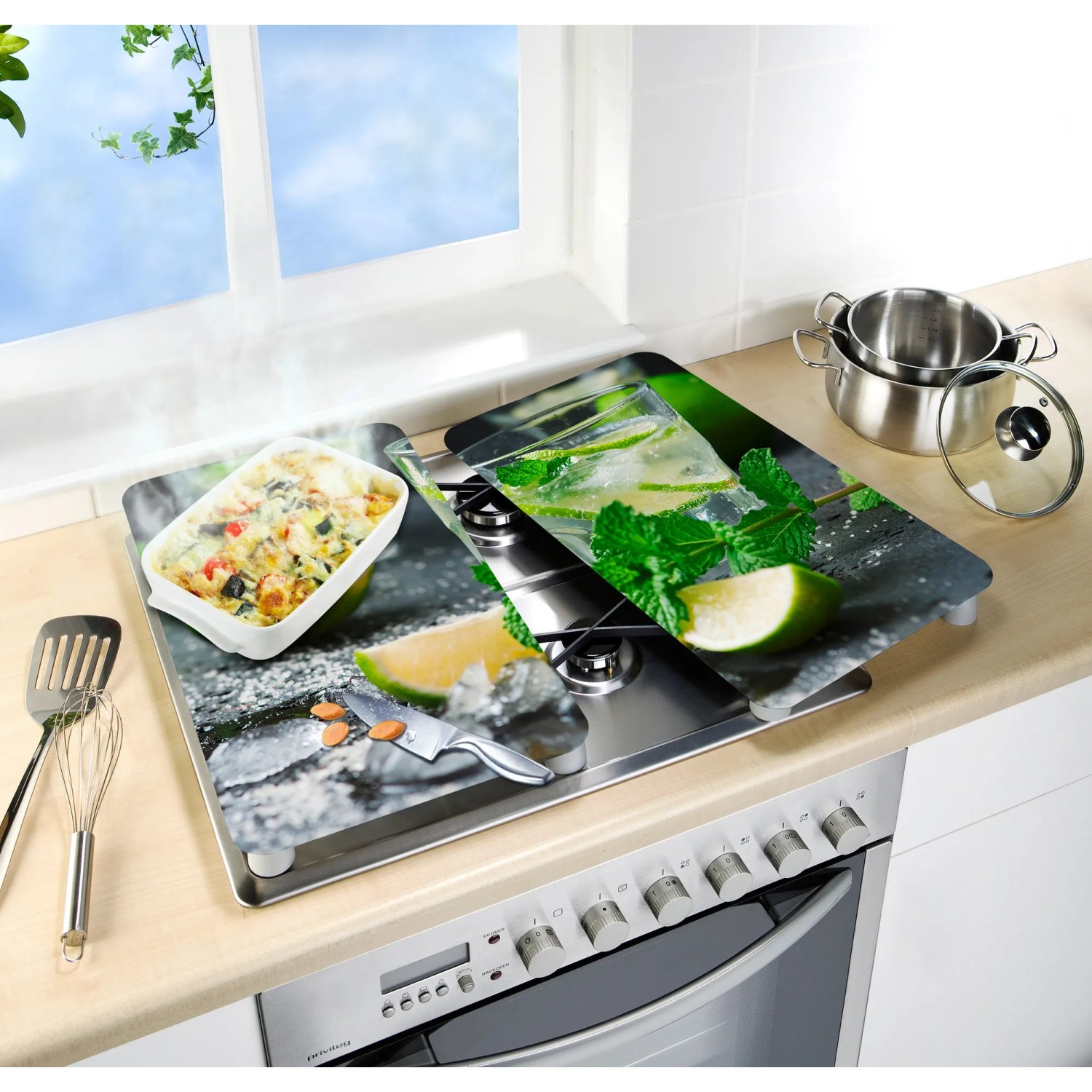 Wenko Herdabdeckplatten Mojito 2er Set auf Herd, mit Cocktail-Motiv und Speisen.
