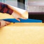 LUX Beschneidelineal 60 cm im Einsatz: Tapete zuschneiden mit Cuttermesser. Tapezierwerkzeug mit blauem Griff.