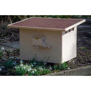 Großer, roter Hummelnistkasten aus Holz mit Bitumendach und Füllmaterial im Garten.