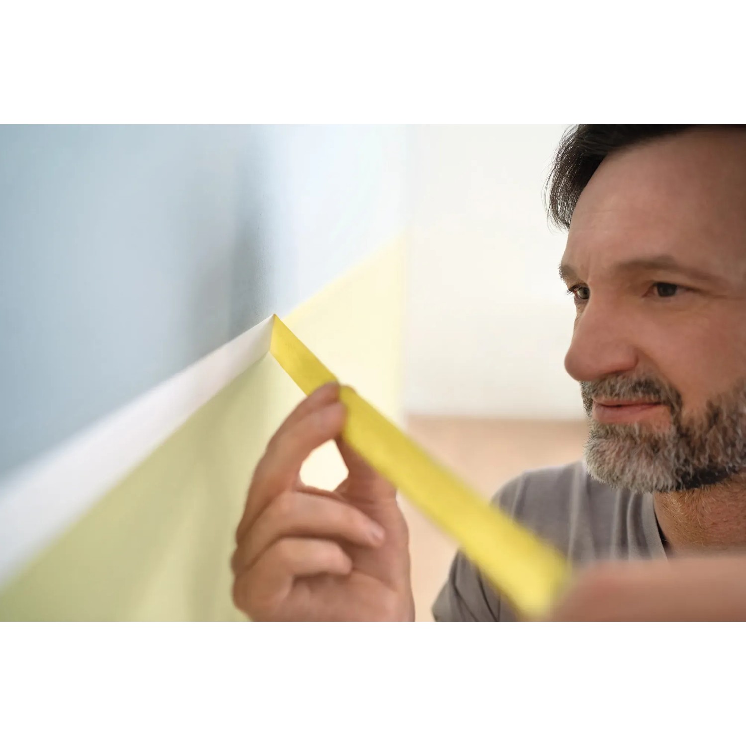 Mann klebt gelbes Tesa Malerband an Wand für präzise Farbkanten.